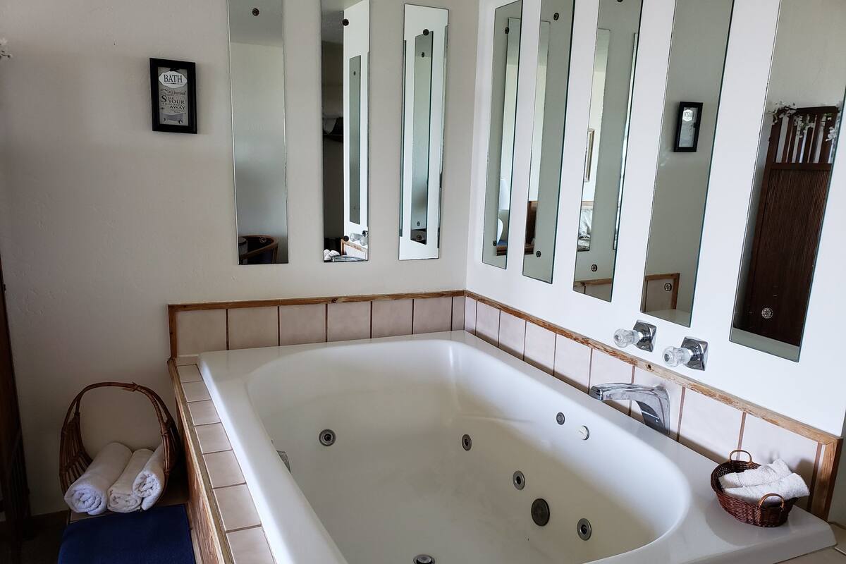 Un baño con una bañera grande, varios espejos y un cartel enmarcado en la pared.