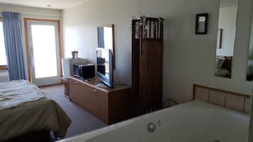 A hotel room with a large bed, a separate bathroom with a bathtub, a television on a wooden dresser, and a mirror on the wall.