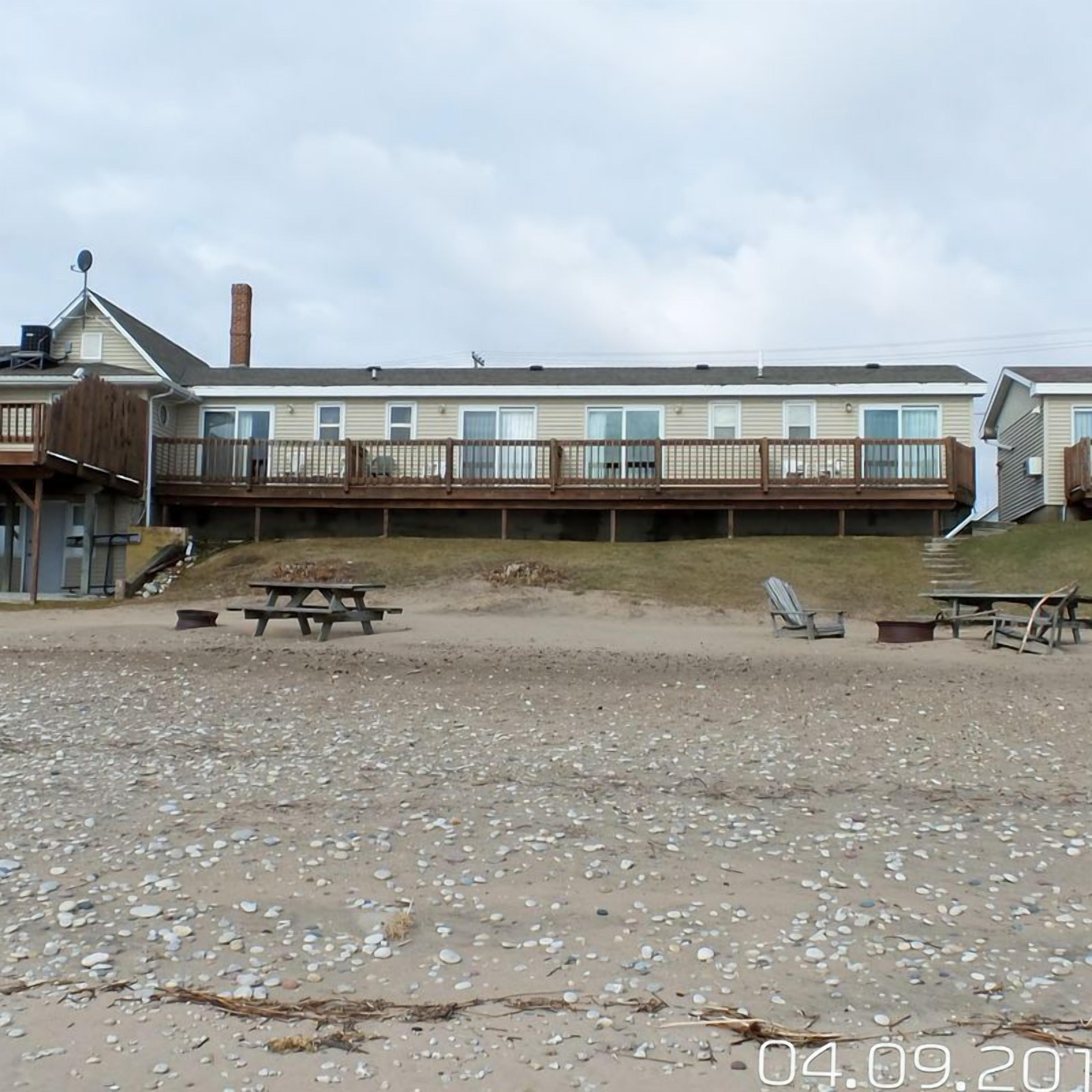 Een vakantiehuis aan het strand met een houten terras, picknicktafels en een klein gebouw.