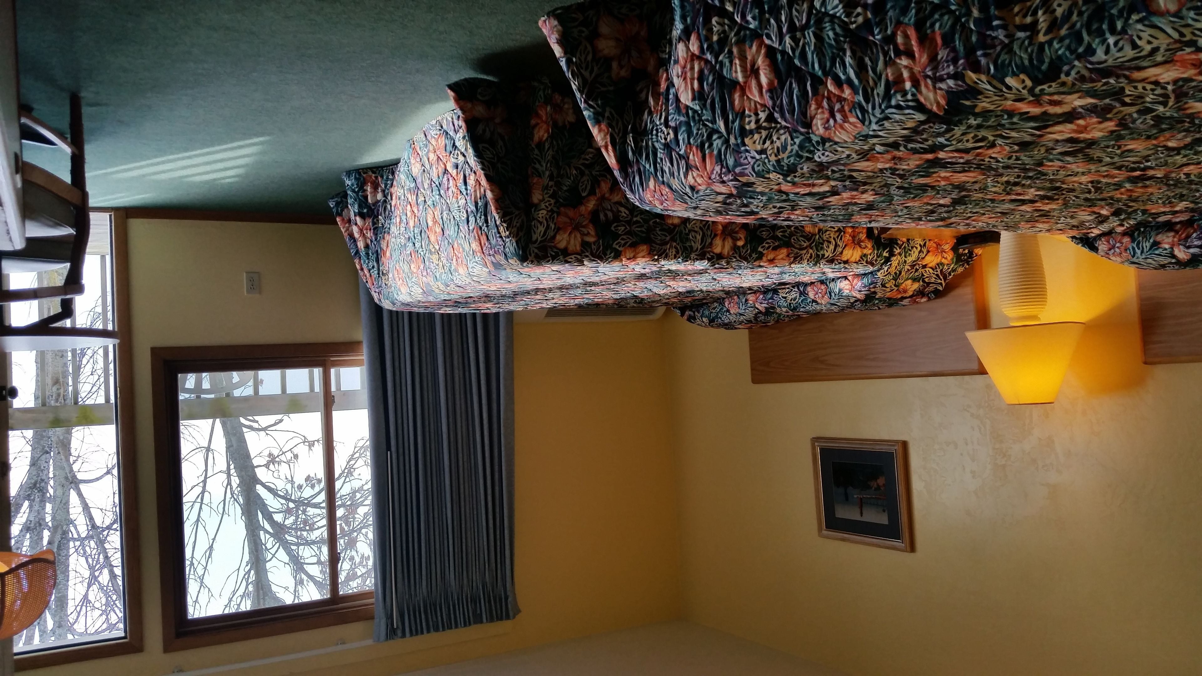 A room with a window, a patterned fabric hanging from the ceiling, a wall-mounted air vent, and a framed picture.