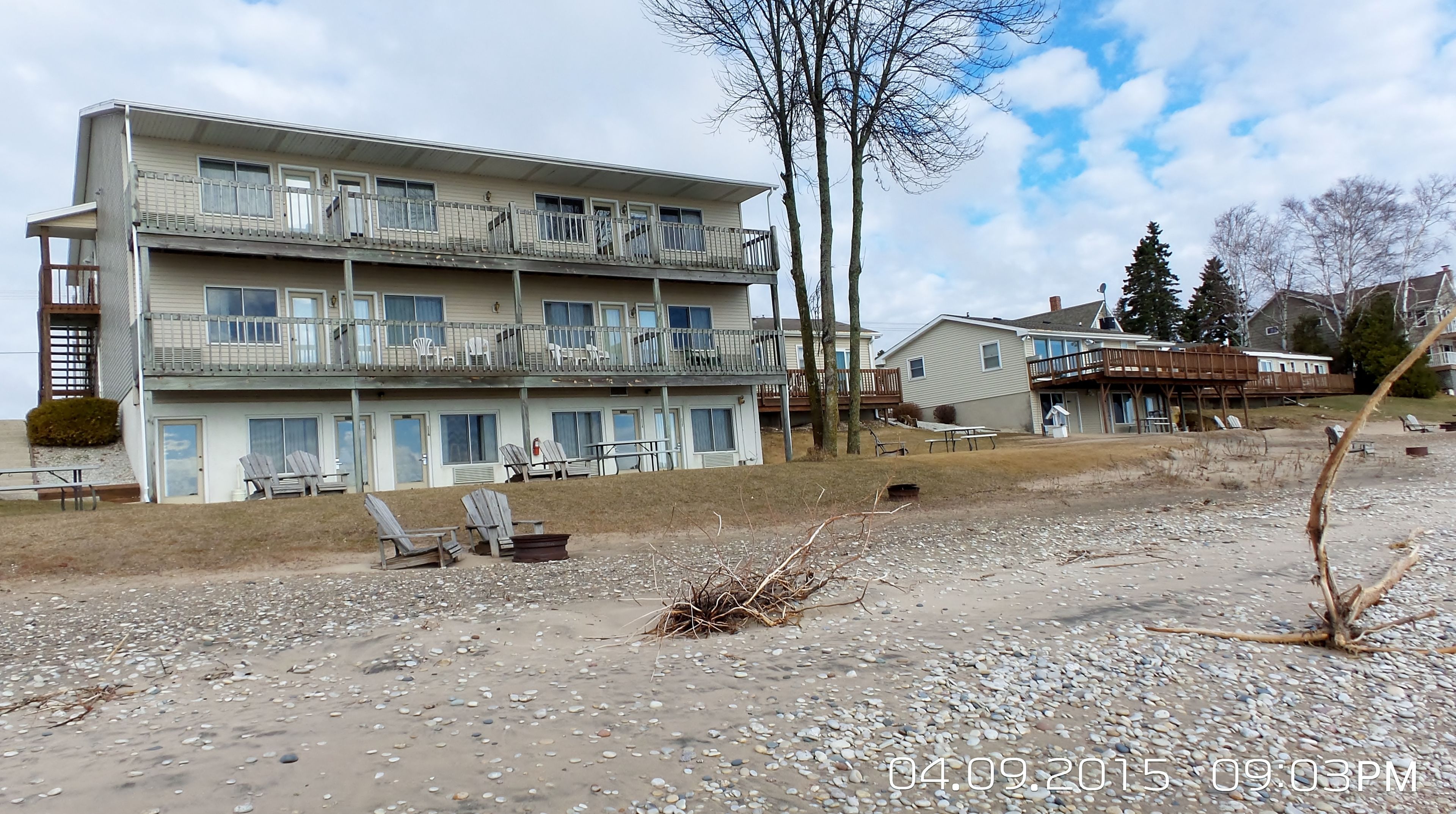A multi-story building with balconies, a sandy ground, and a clear sky.