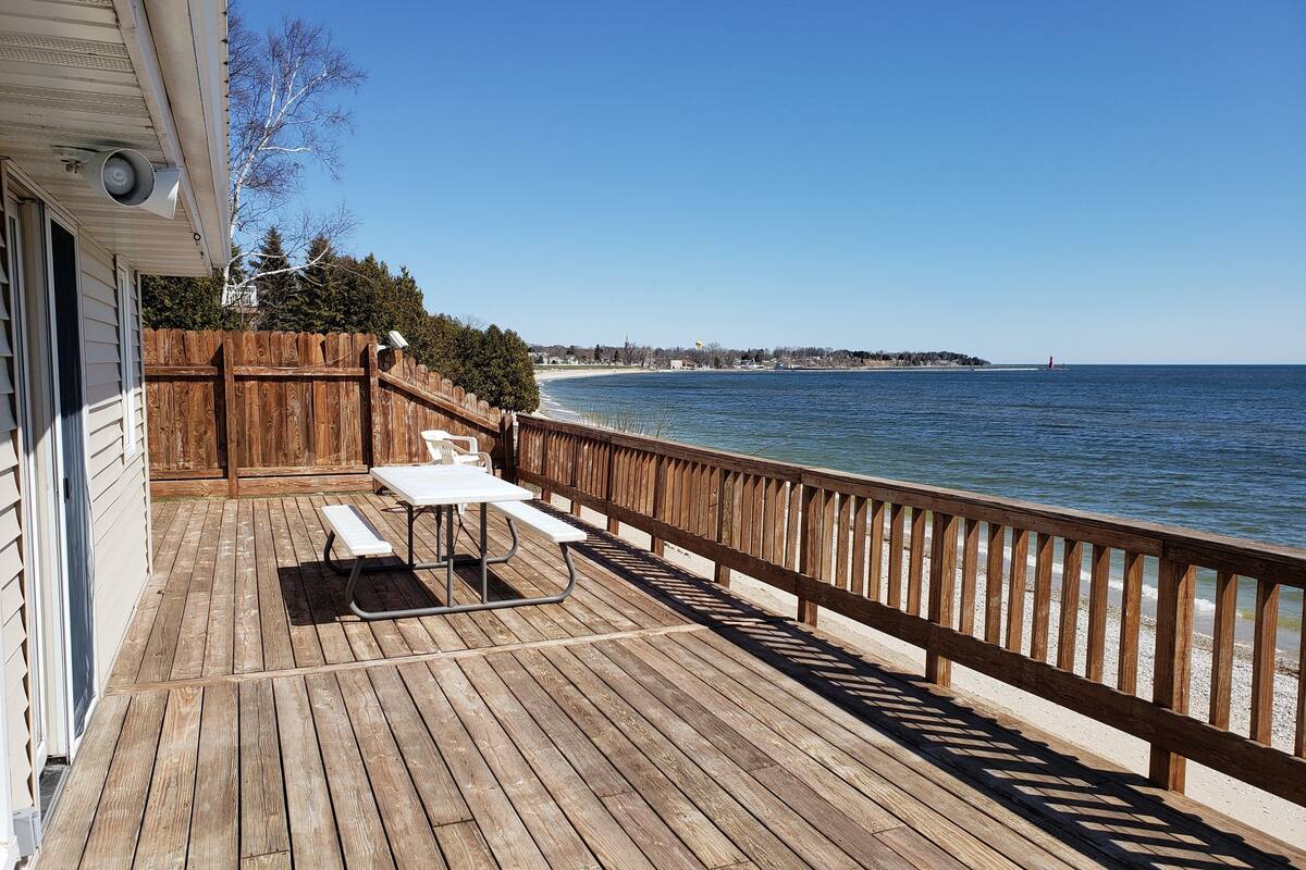 Una terraza de madera con mesas de picnic y barandilla con vista a la playa.