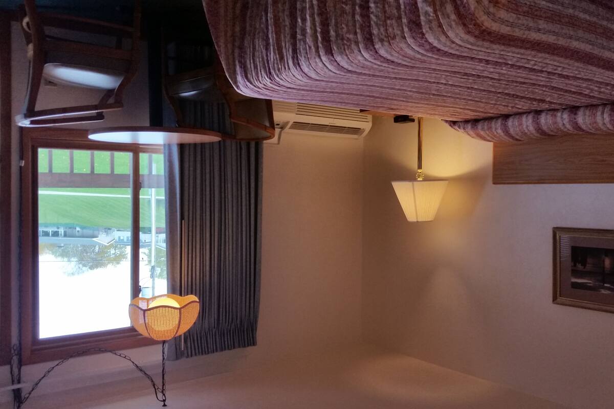 Una habitación con un ventanal grande, un lámpara colgante y un equipo de aire acondicionado instalado en la pared.