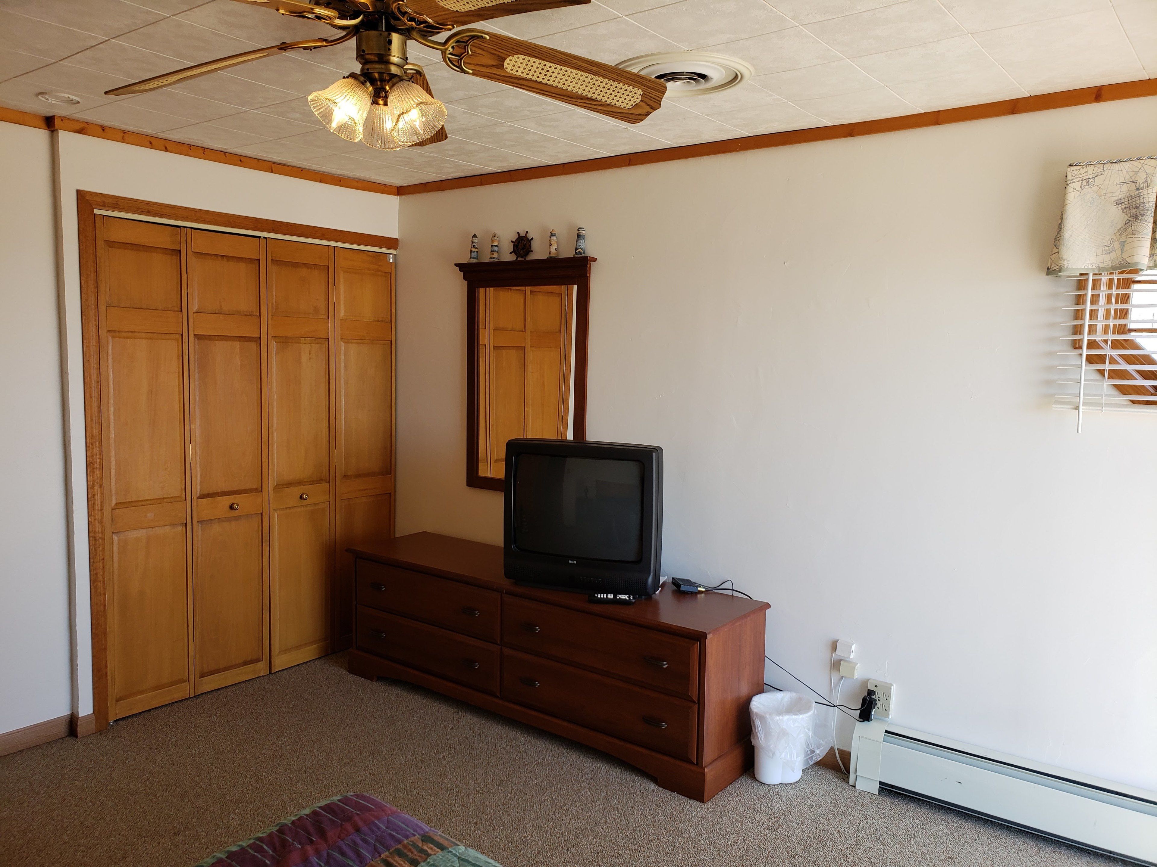 Een slaapkamer met een houten garderobe, een dressoir, een televisie, een plafondventilator en een radiator.