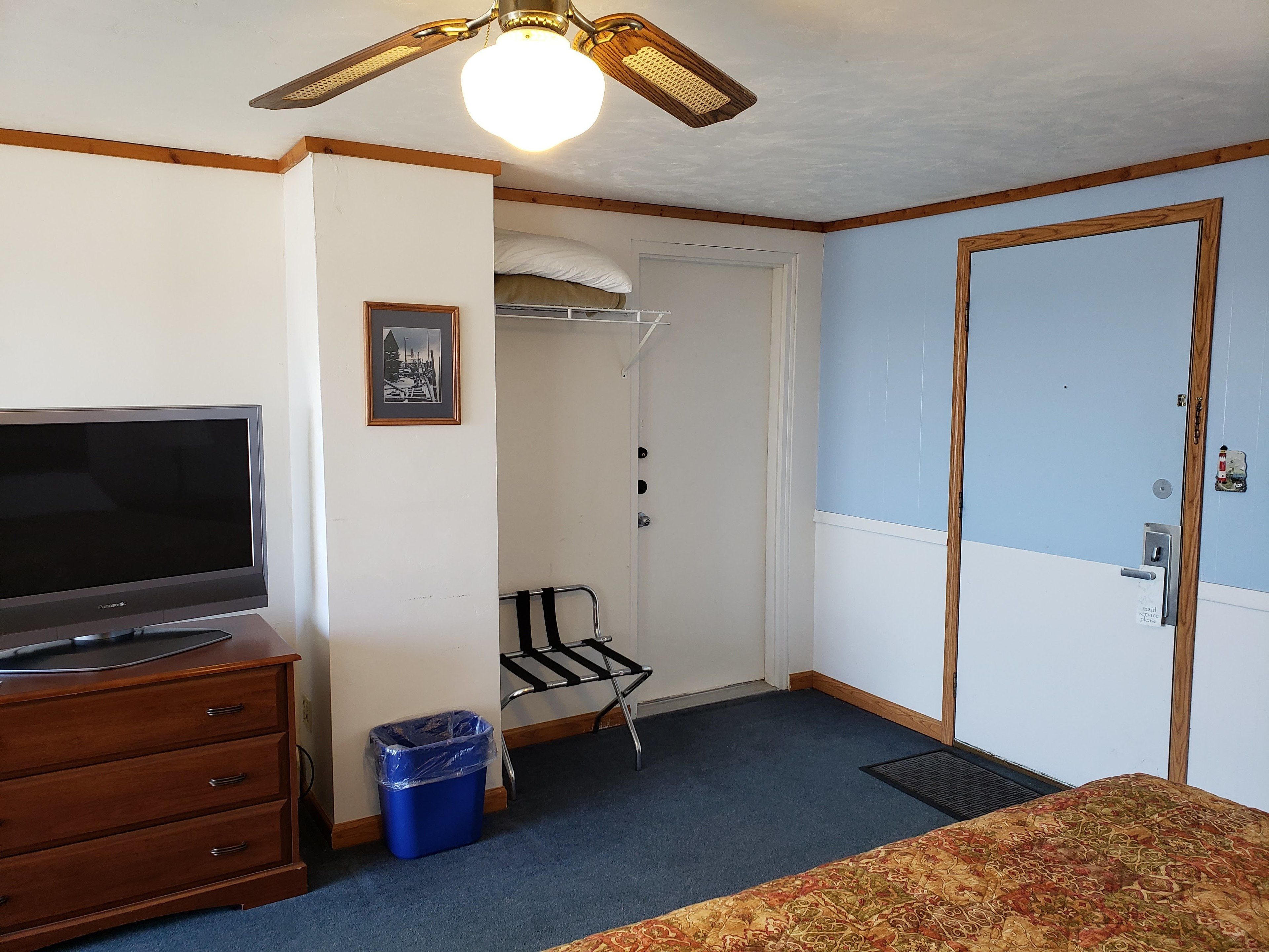 A room with a television on a wooden dresser, a blue trash bin, a coat rack, and a door with a sign.