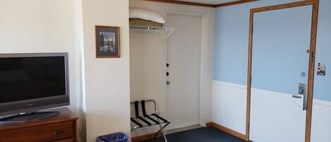 A room with a television on a wooden dresser, a blue trash bin, a coat rack, and a door with a sign.