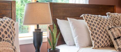 A neatly made bed with patterned pillows, a bedside lamp, and a potted plant.