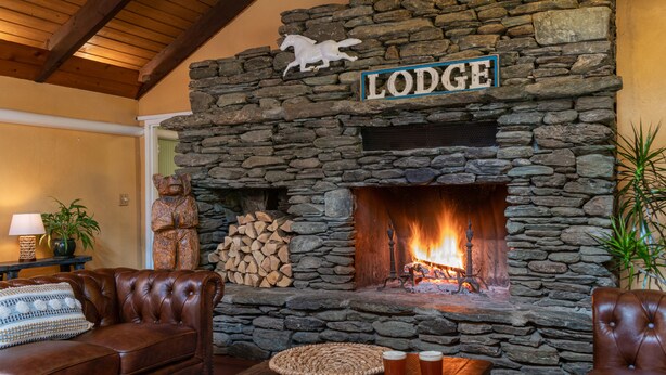 Une cheminée en pierre surmontée d’une enseigne indiquant « Lodge », une statue d’ours et une table en bois avec des collations et des boissons.