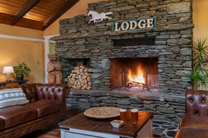 A stone fireplace with a sign reading "Lodge" above it, a bear statue, and a wooden table with snacks and drinks. - White Horse Lodge (Waitsfield)