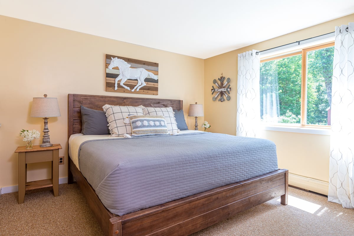 A bedroom with a wooden bed, two nightstands, a window with curtains, and a wall-mounted horse decoration.