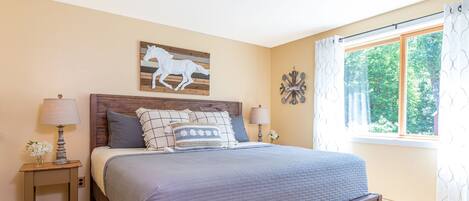 A bedroom with a wooden bed, two nightstands, a window with curtains, and a wall-mounted horse decoration.
