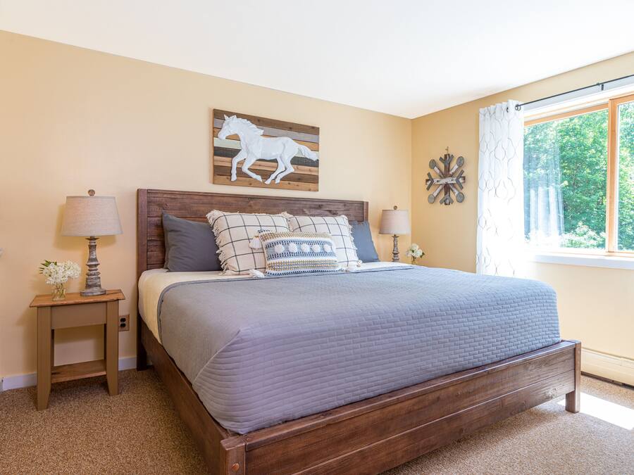 Une chambre à coucher avec un lit en bois, deux tables de chevet, une fenêtre avec des rideaux et une décoration murale représentant un cheval.