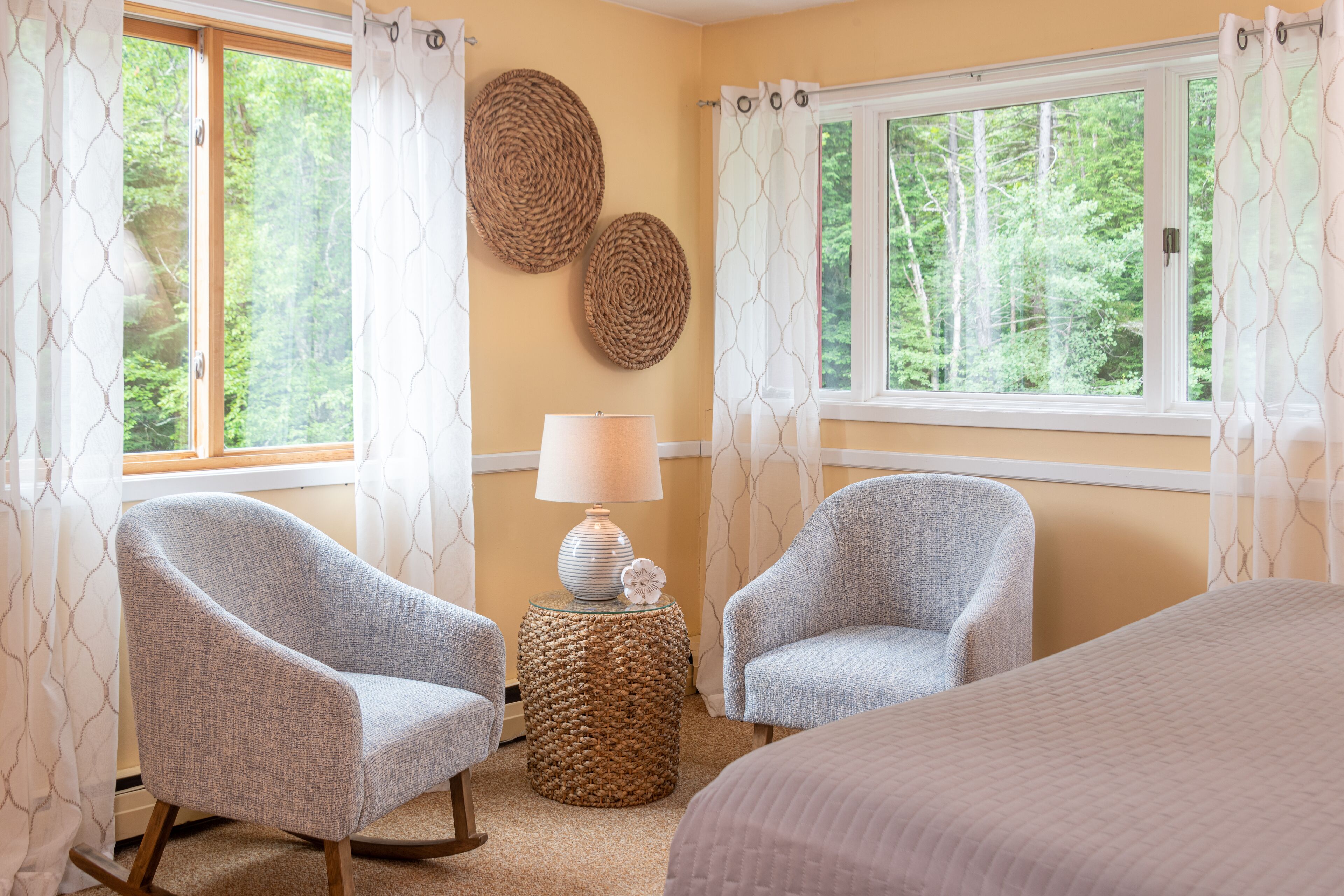 A bedroom with two rocking chairs, a lamp on a round side table, and a bed.