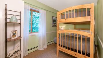 A child's bunk bed room with a window, a shelf with decorative items, and a framed picture on the wall.