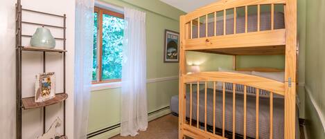 Une chambre pour enfant avec un lit superposé, une fenêtre, une étagère avec des objets décoratifs et un tableau encadré au mur.