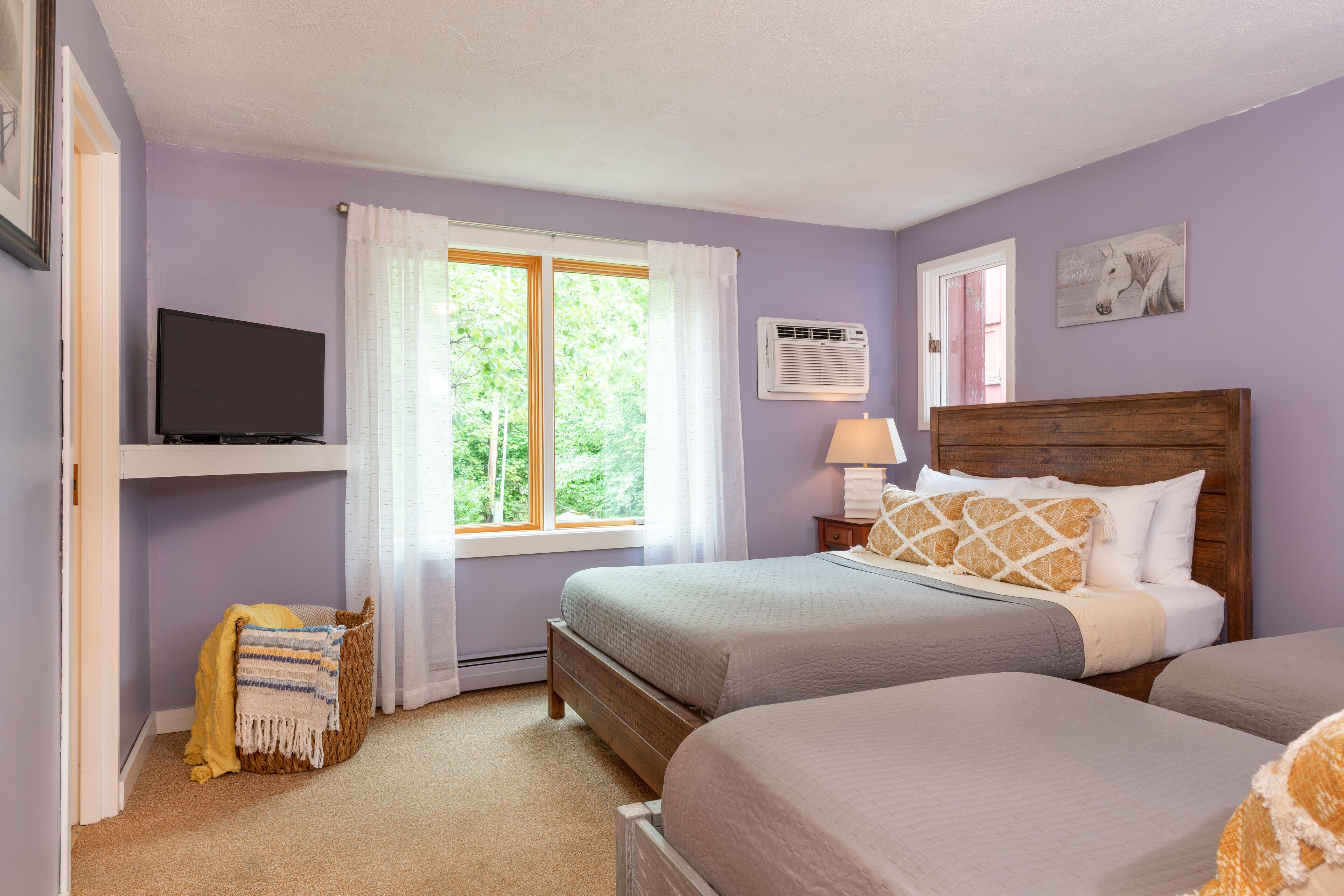 A bedroom with two beds, a television, a window with curtains, and a wall-mounted air conditioner.