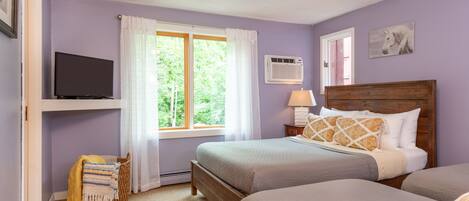 A bedroom with two beds, a television, a window with curtains, and a wall-mounted air conditioner.