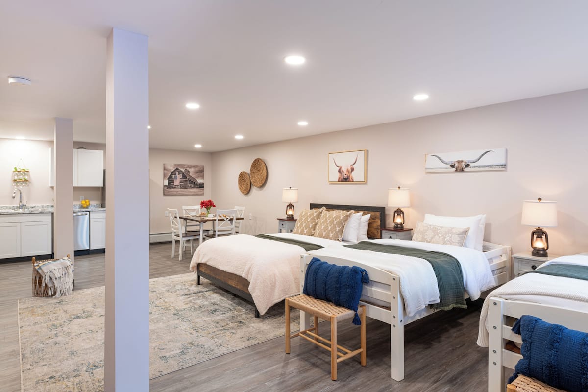 A modern hotel room with a large bed, a smaller bed, a desk, and a dining area.