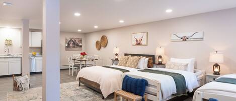 A modern hotel room with a large bed, a smaller bed, a desk, and a dining area.