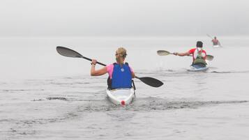 Un kayakista con chaleco salvavidas azul rema en un kayak blanco sobre una masa de agua brumosa.