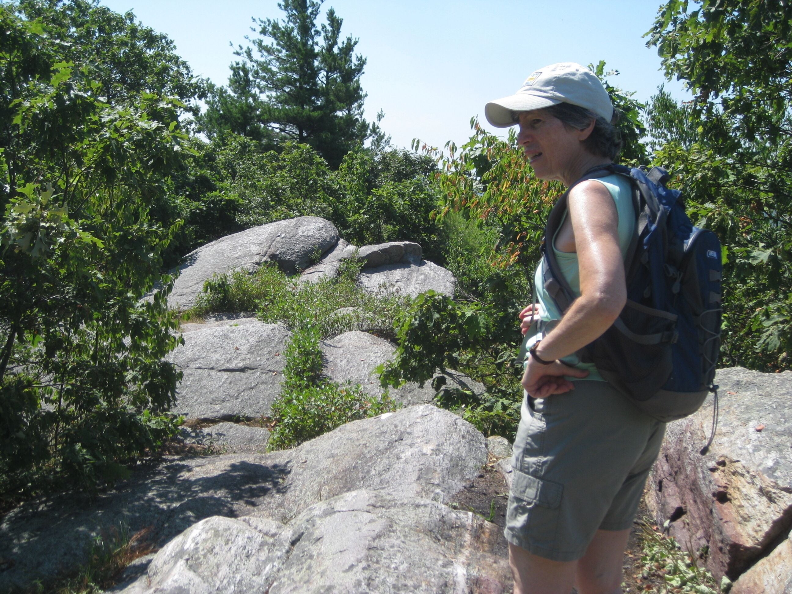 Una persona camina con una mochila, rodeada de rocas grandes y vegetación densa.