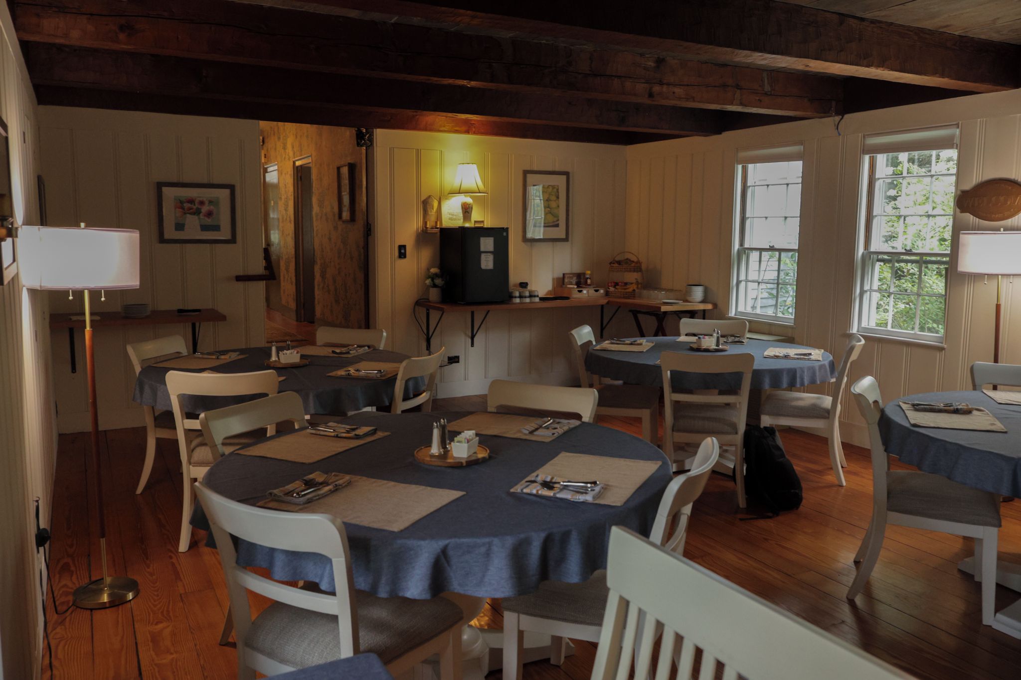 A dining area with round tables, chairs, and a kitchen counter with a refrigerator.