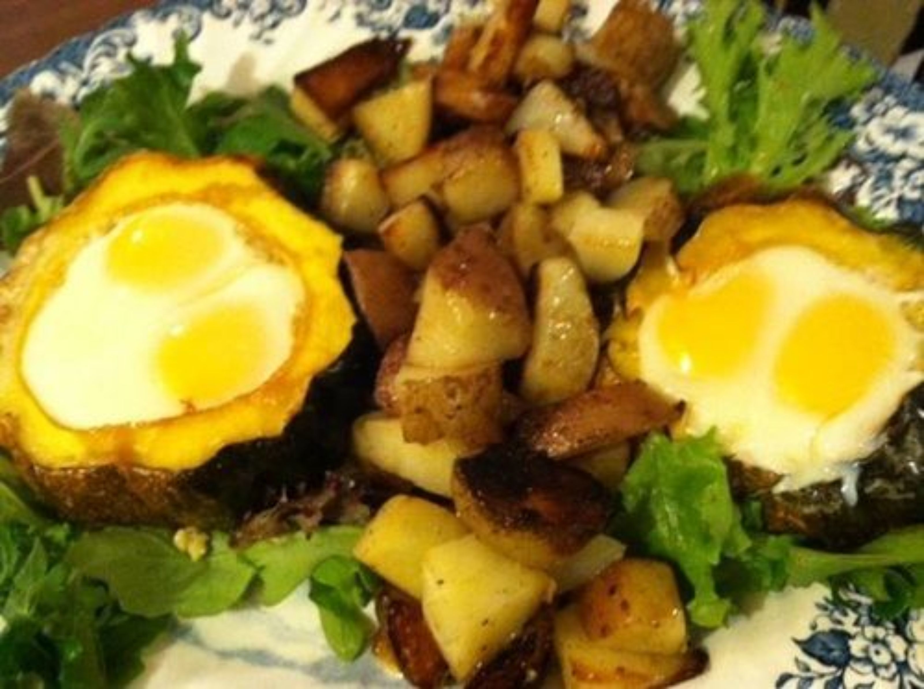A plate with a salad, roasted potatoes, and two halves of an egg.