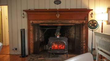 A room with a fireplace, a standing heater, and a fan.