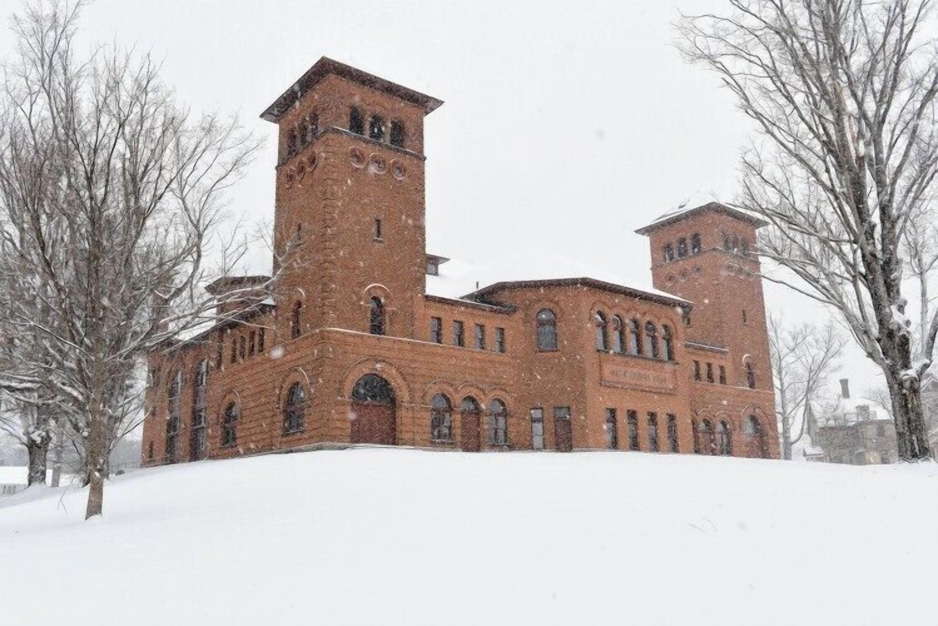 A large brick building with two towers and arched windows, surrounded by snow.