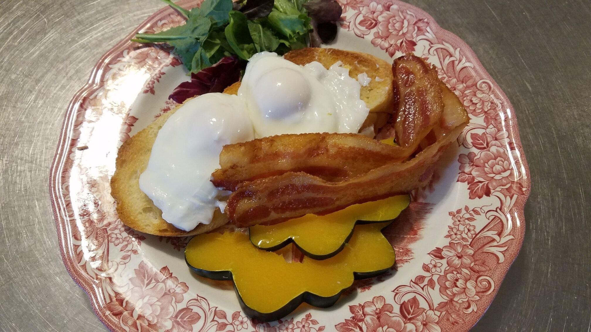 A plate with a poached egg, bacon, toast, and a slice of yellow cheese.