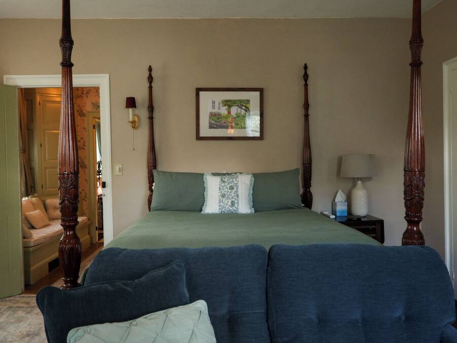 A four-poster bed with a green bedspread and a decorative pillow, a framed picture on the wall, and a bedside table with a lamp.