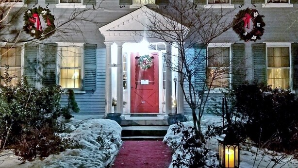 A two-story house with a red door, green shutters, and a snow-covered front yard. - Centennial House (Northfield)