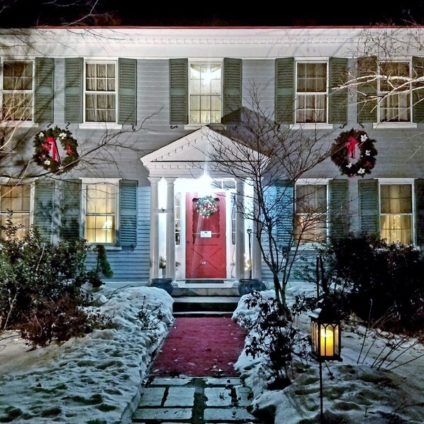 A two-story house with a red door, green shutters, and a snow-covered front yard. - Centennial House (Northfield)