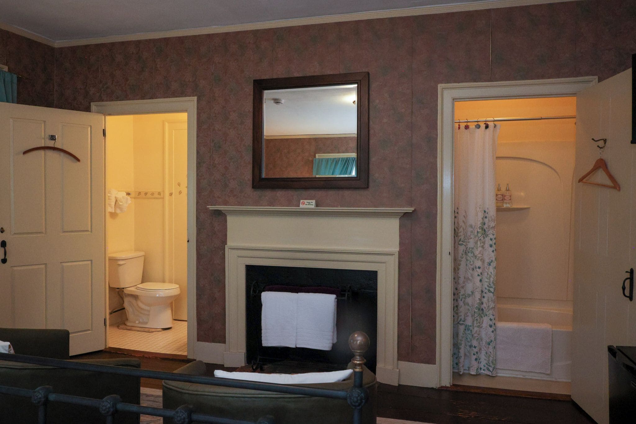 A room with a fireplace, a mirror above it, a door leading to a bathroom, and a bed with a headboard.