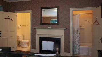 A room with a fireplace, a mirror above it, a door leading to a bathroom, and a bed with a headboard.