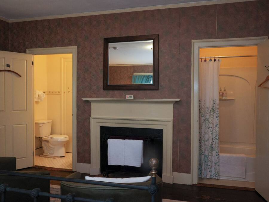 A room with a fireplace, a mirror above it, a door leading to a bathroom, and a bed with a headboard.