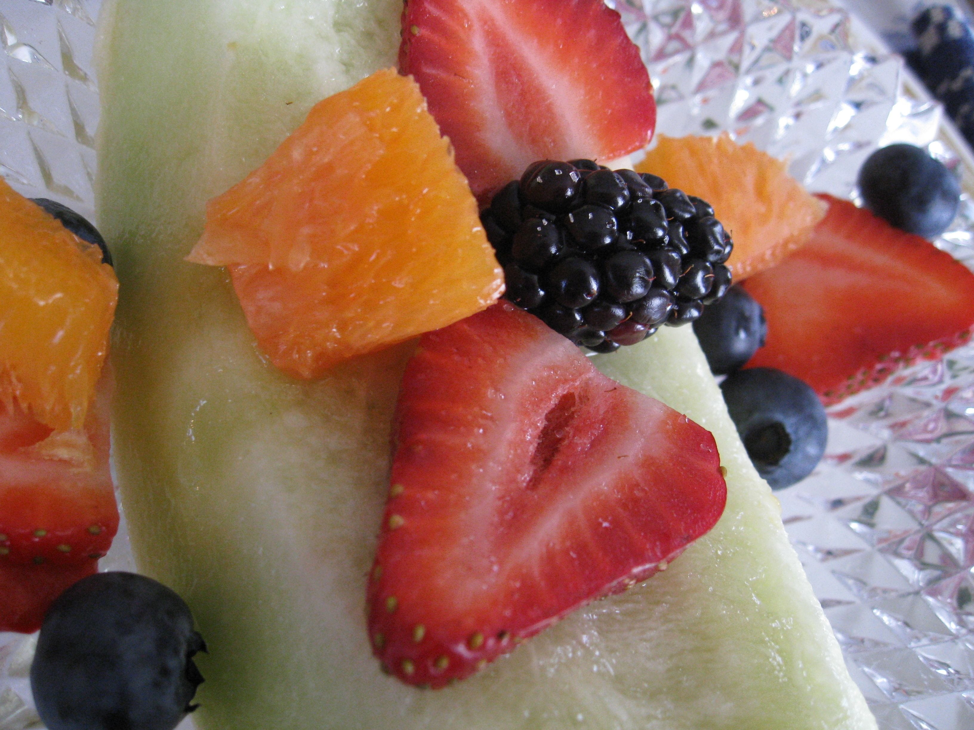 A close-up of a fruit arrangement with strawberries, blackberries, and orange slices on a glass surface.