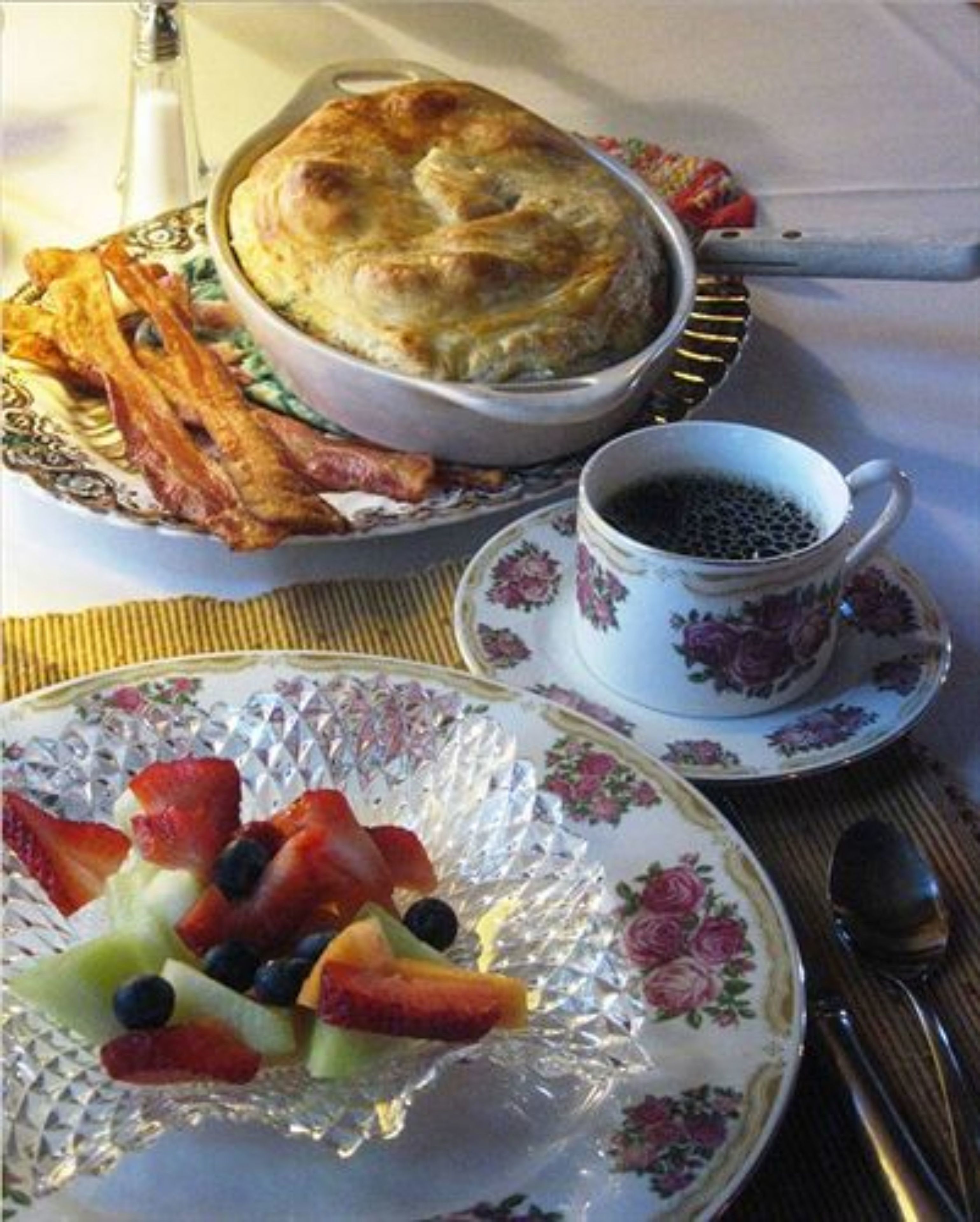 Desayuno con un pastel de ricota, tocino, fruta y café.