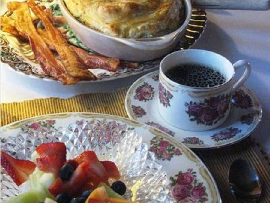 Desayuno con un pastel de ricota, tocino, fruta y café.