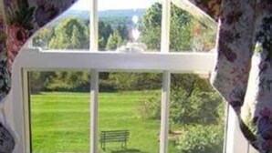 A window with a view of a grassy field and a bench. - Centennial House (Northfield)