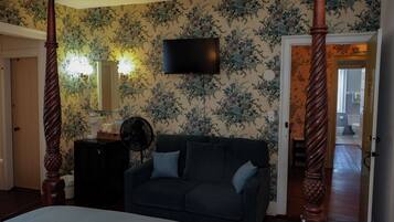 Un dormitorio con una cama con dosel, un televisor de pantalla plana montado en la pared, un sofá de color oscuro y un aparador de madera.