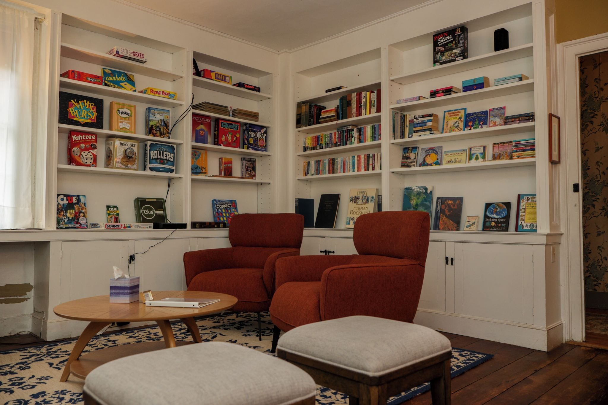 A cozy reading nook with a fireplace, a comfortable armchair, a small table, and a bookshelf filled with various board games and books.