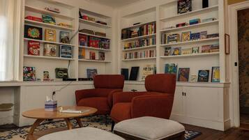 A cozy reading nook with a fireplace, a comfortable armchair, a small table, and a bookshelf filled with various board games and books.