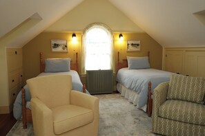 A bedroom with two beds, a radiator, a window with curtains, and a chair. - Centennial House (Northfield)