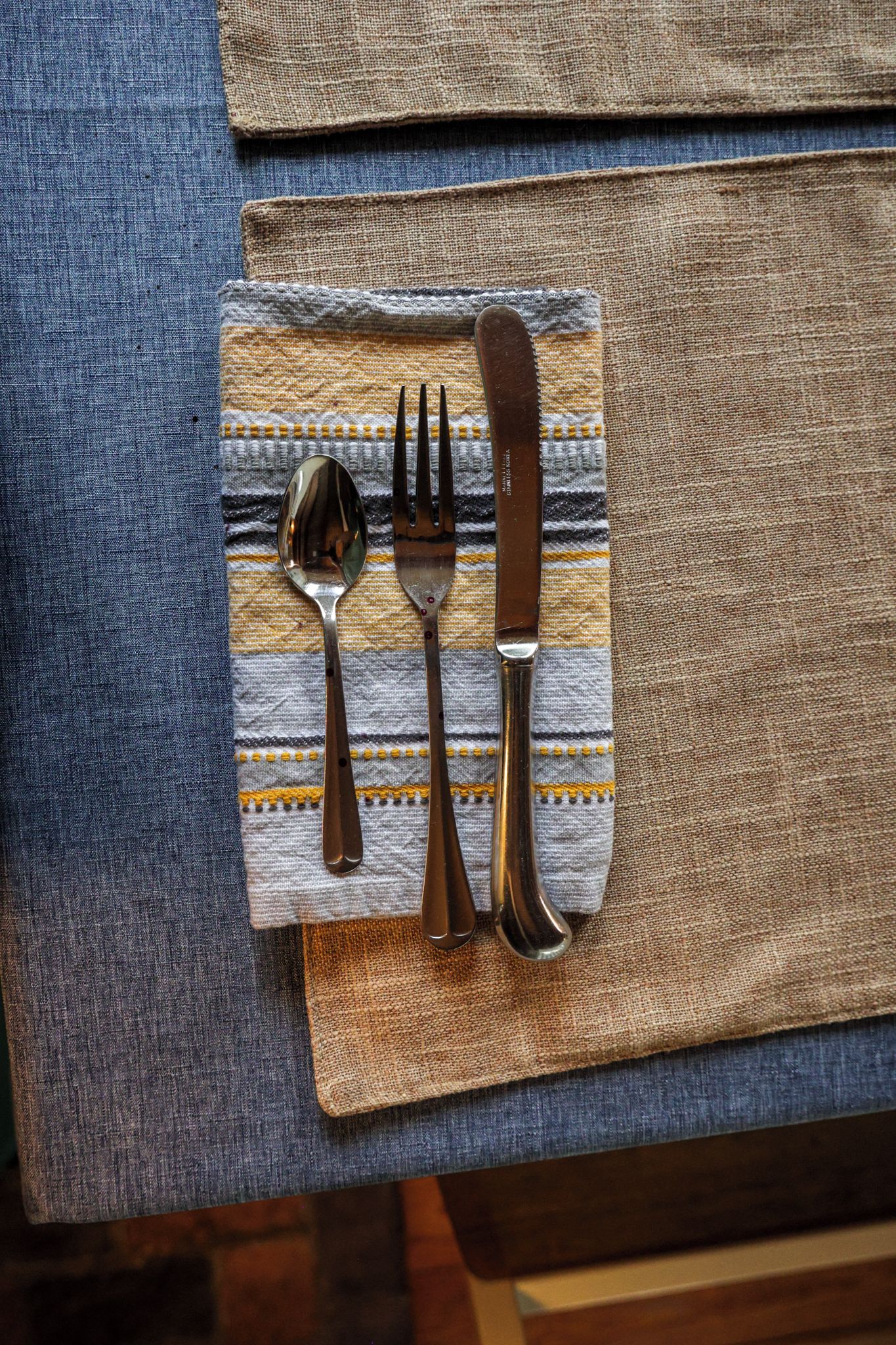 A table setting with a blue tablecloth, a striped napkin, and cutlery.