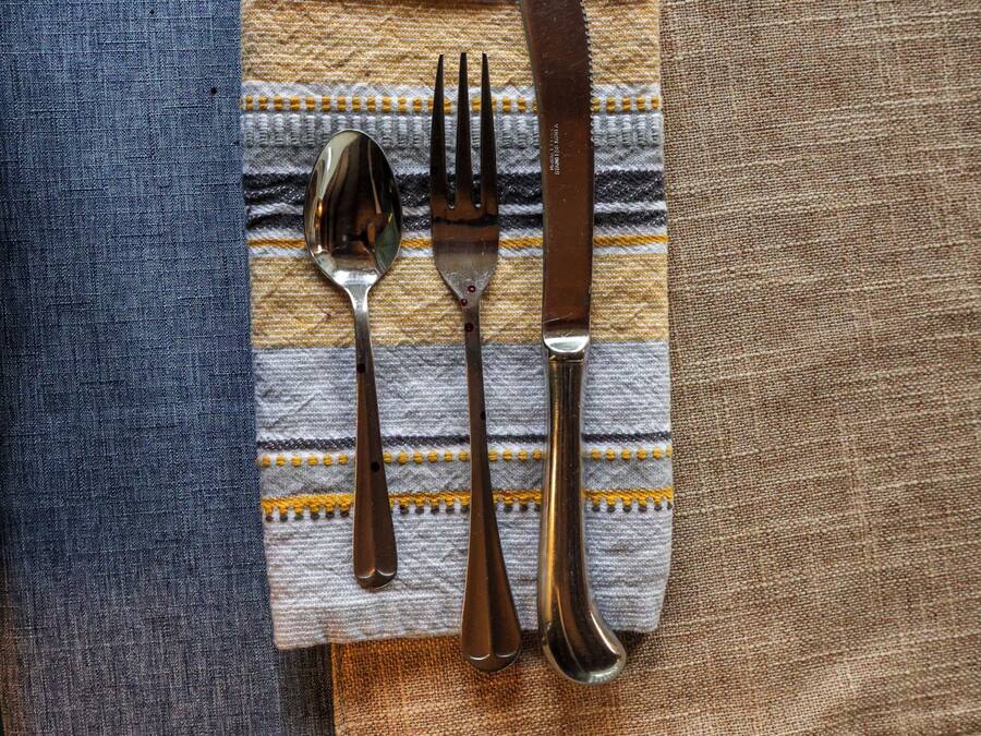 A table setting with a blue tablecloth, a striped napkin, and cutlery.