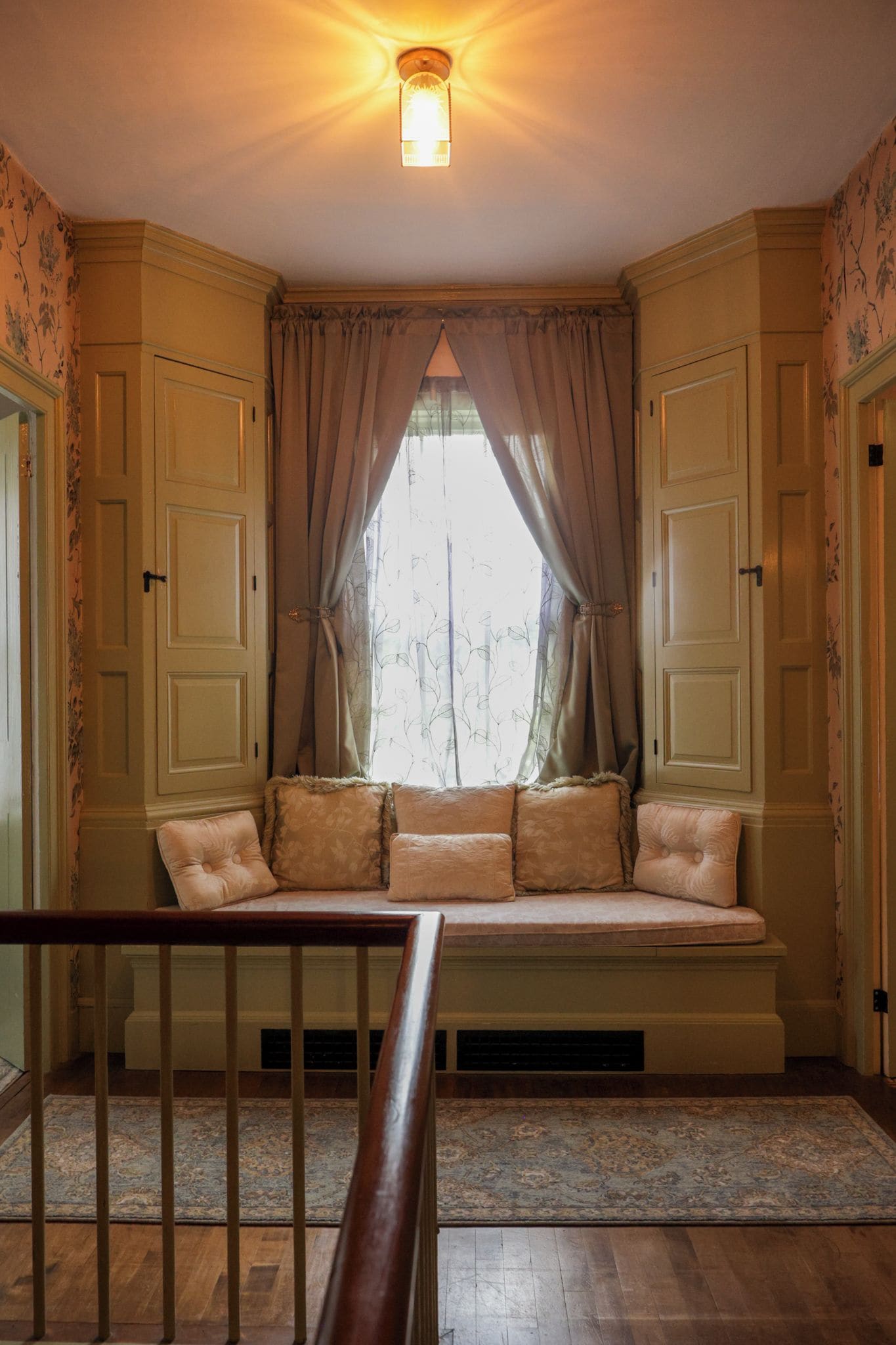 Una habitación con un banco empotrado, una ventana con cortinas y una barandilla de madera.