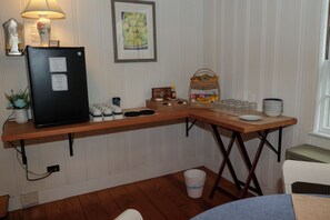 Une petite cuisine équipée d’un réfrigérateur, d’un coin café et d’un panier de fruits.