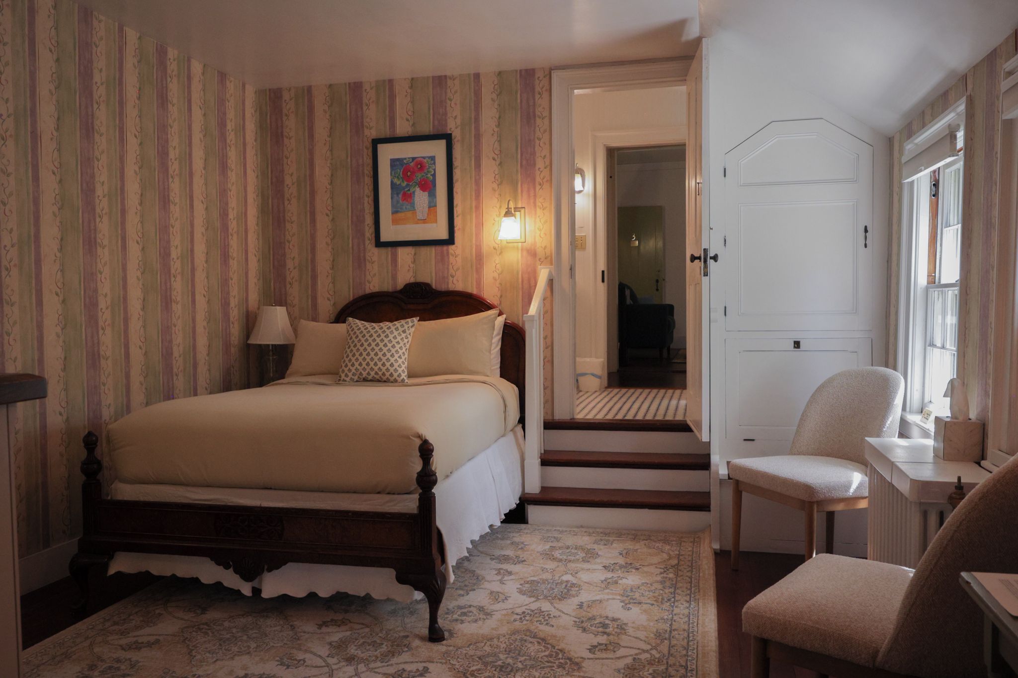 A bedroom with a bed, a nightstand, a lamp, a chair, and a door leading to another room.