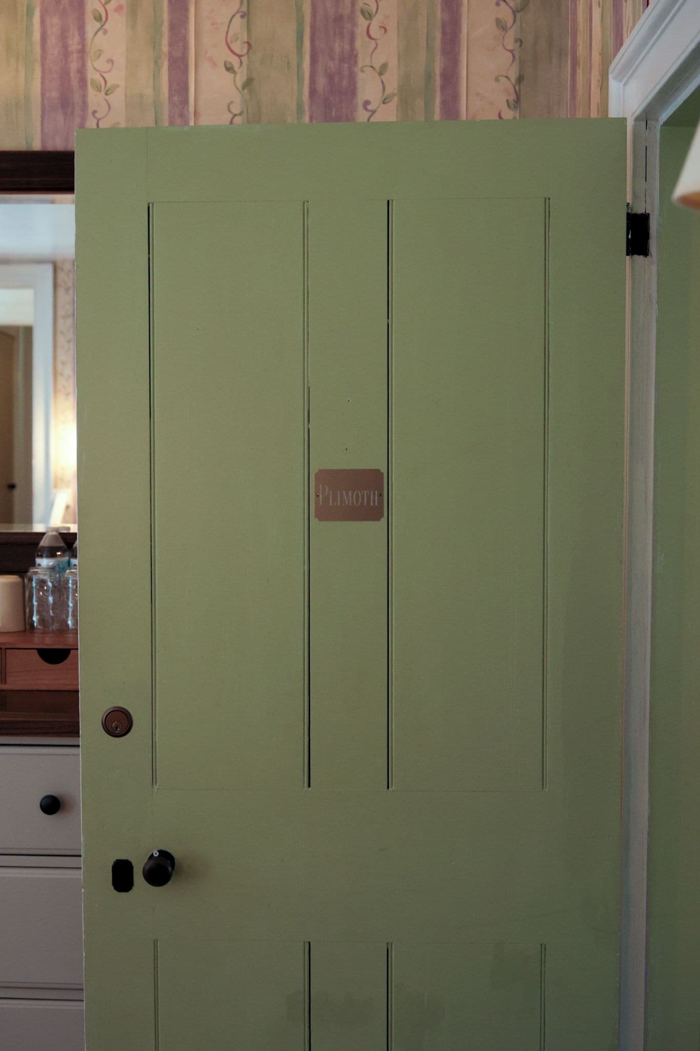 Una puerta verde con una etiqueta que dice 'PLIMOTH' y una cerradura.